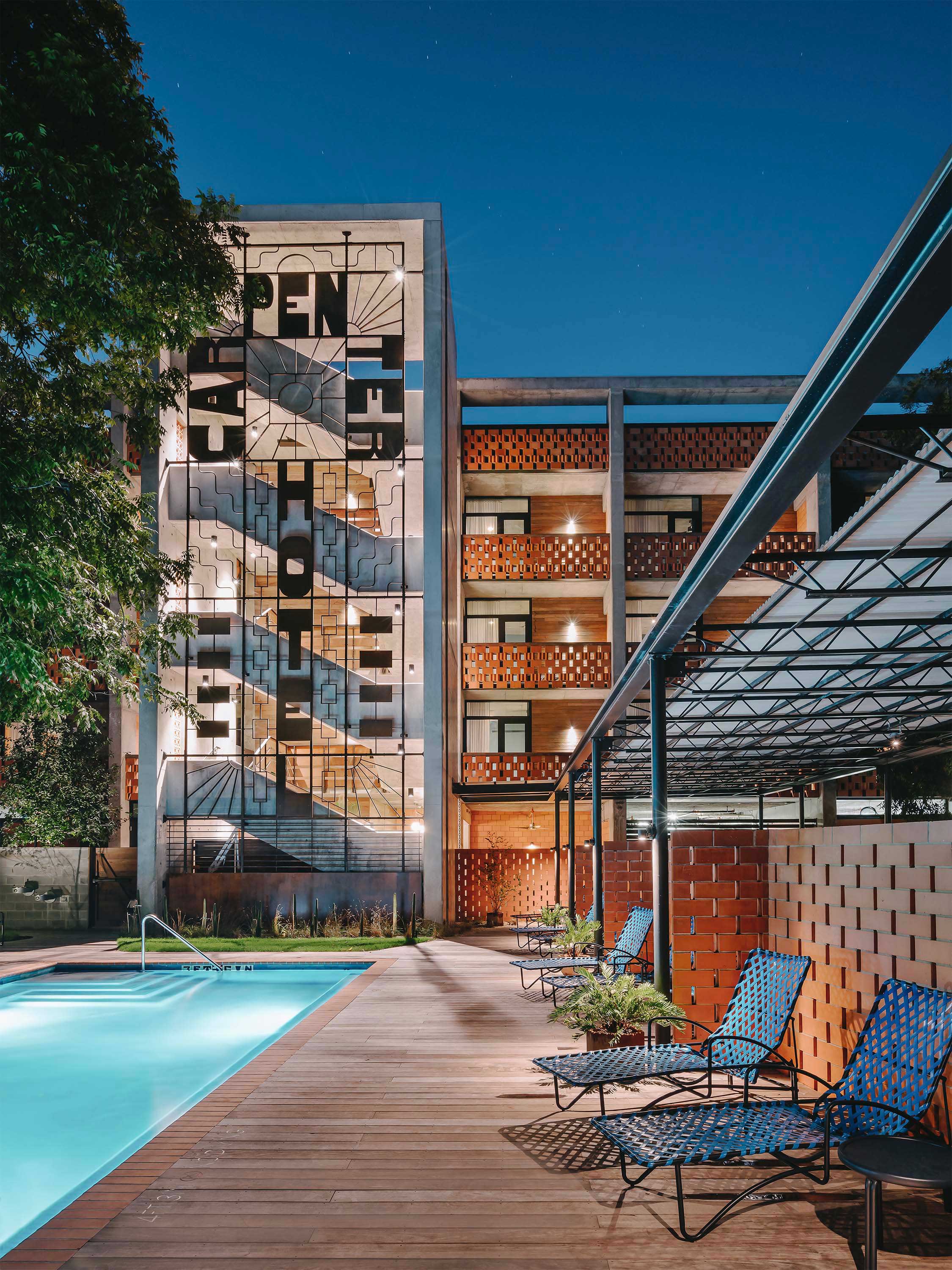 Exterior photo of the Carpenter Hotel by Specht Novak Architects. Shot by Chase Daniel, featuring the pool, lounging area surrounded by trees, and the hotel structure in the background.